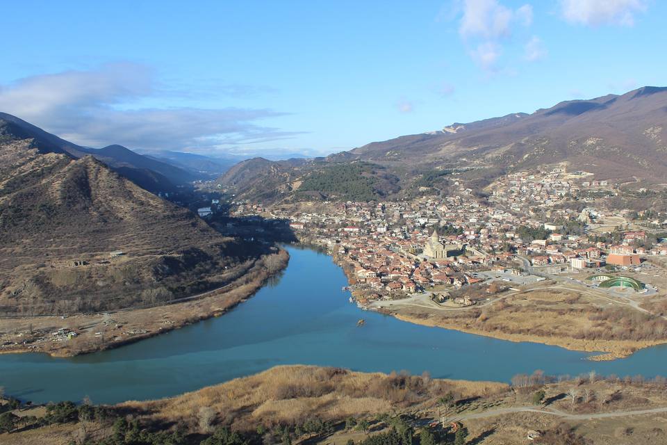 View from Jvari Monastery over Mtskheta, Georgia: the blue Aragvi and Mtkvari rivers meet below the old town and Svetitskhoveli Cathedral, with winter-brown hills under a clear sky